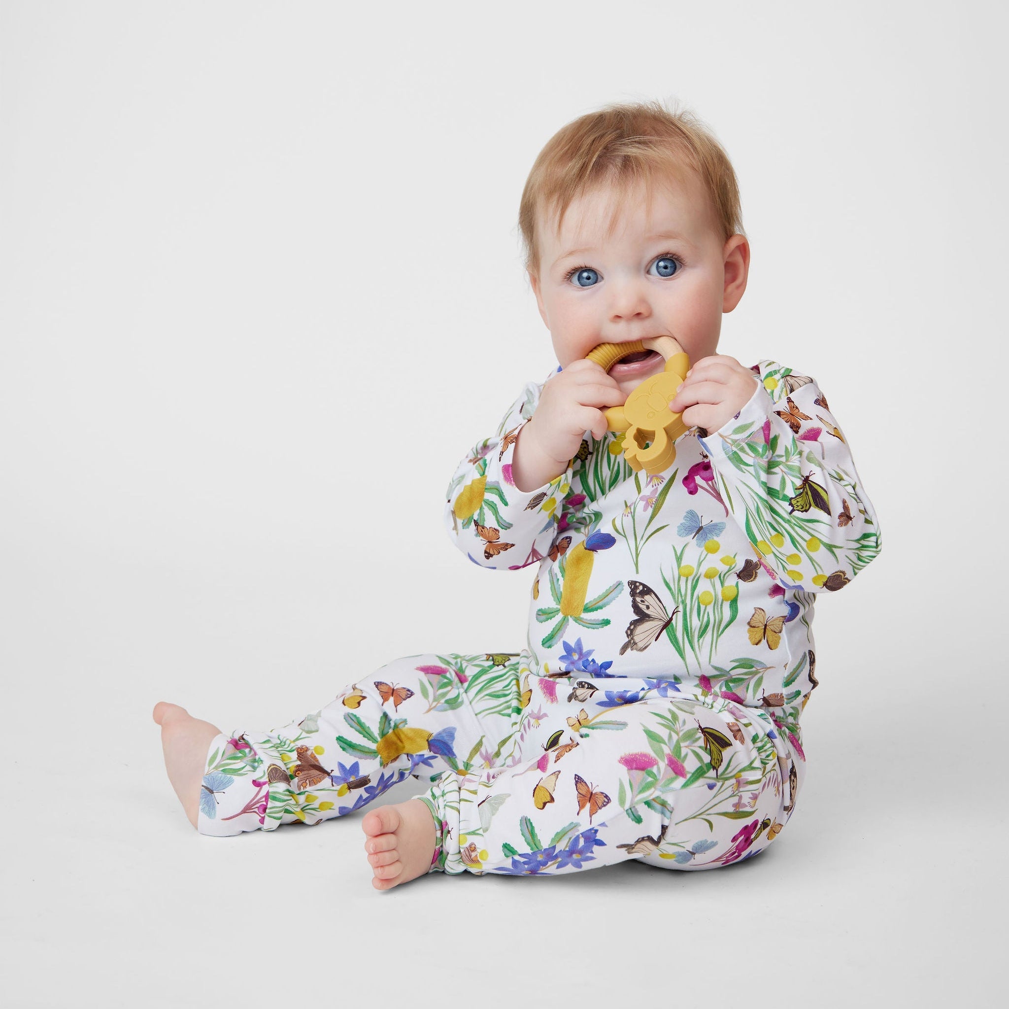 Baby sitting in Butterfly Flora Australian made organic cotton romper while chewing a teether toy.