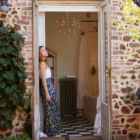 Woman standing in a doorway of a stone-walled house, looking into the room.