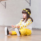 Child sitting on the floor wearing a yellow and white outfit with flower headband.
