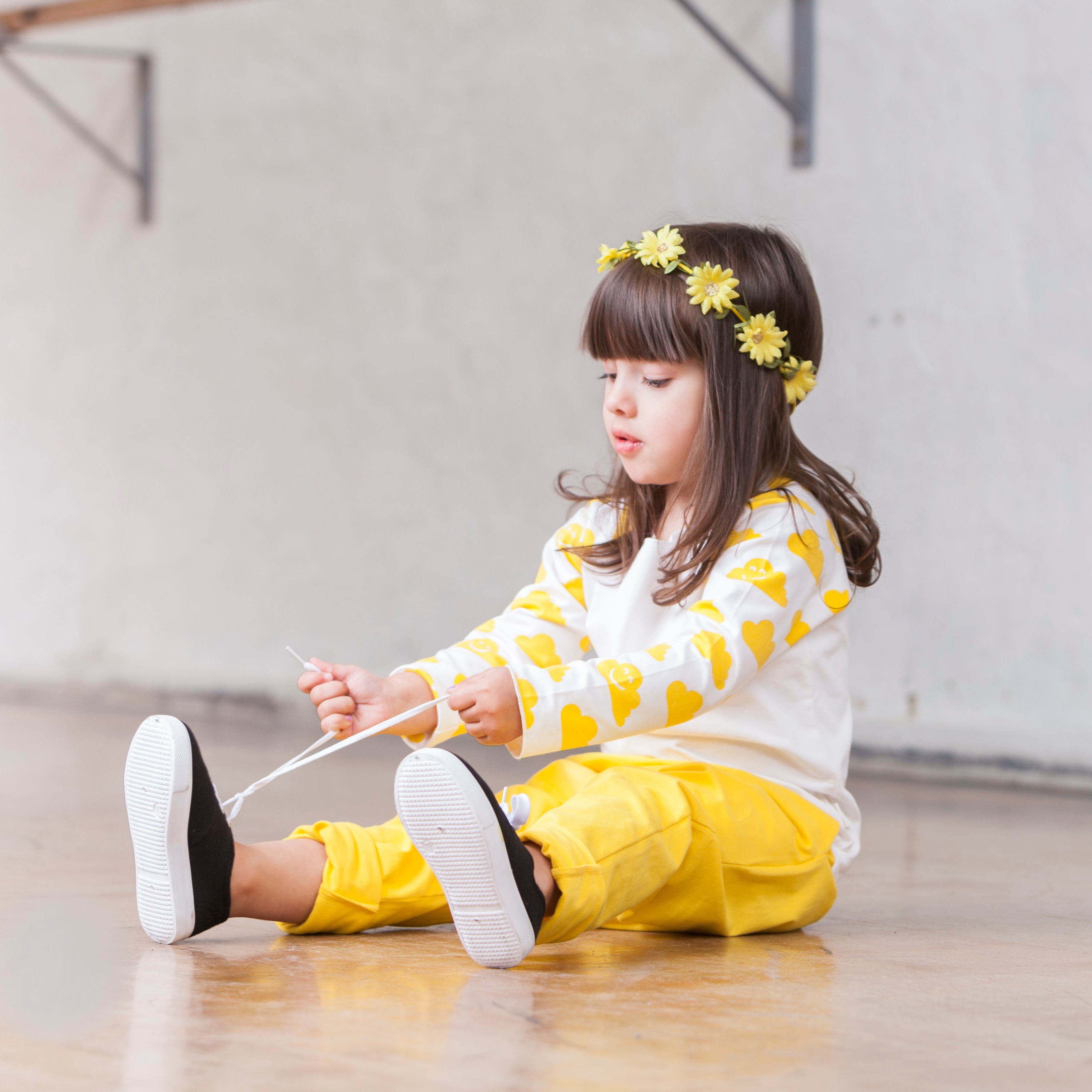 Child sitting on the floor wearing a yellow and white outfit with flower headband.