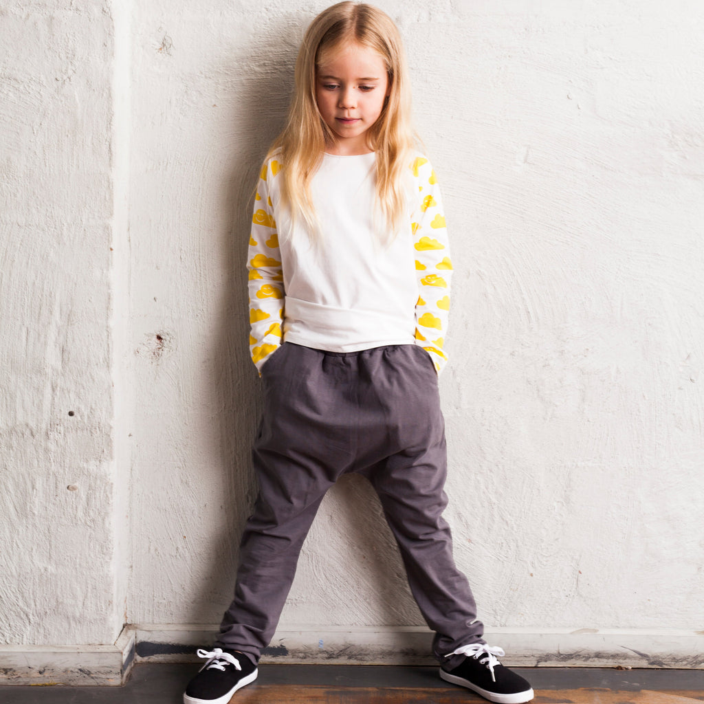 Child wearing a yellow and white striped sweater and gray pants against a white wall.