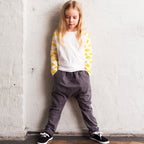 Child wearing a yellow and white striped sweater and gray pants against a white wall.