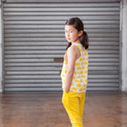 Young girl in yellow outfit standing in front of a gray shutter.