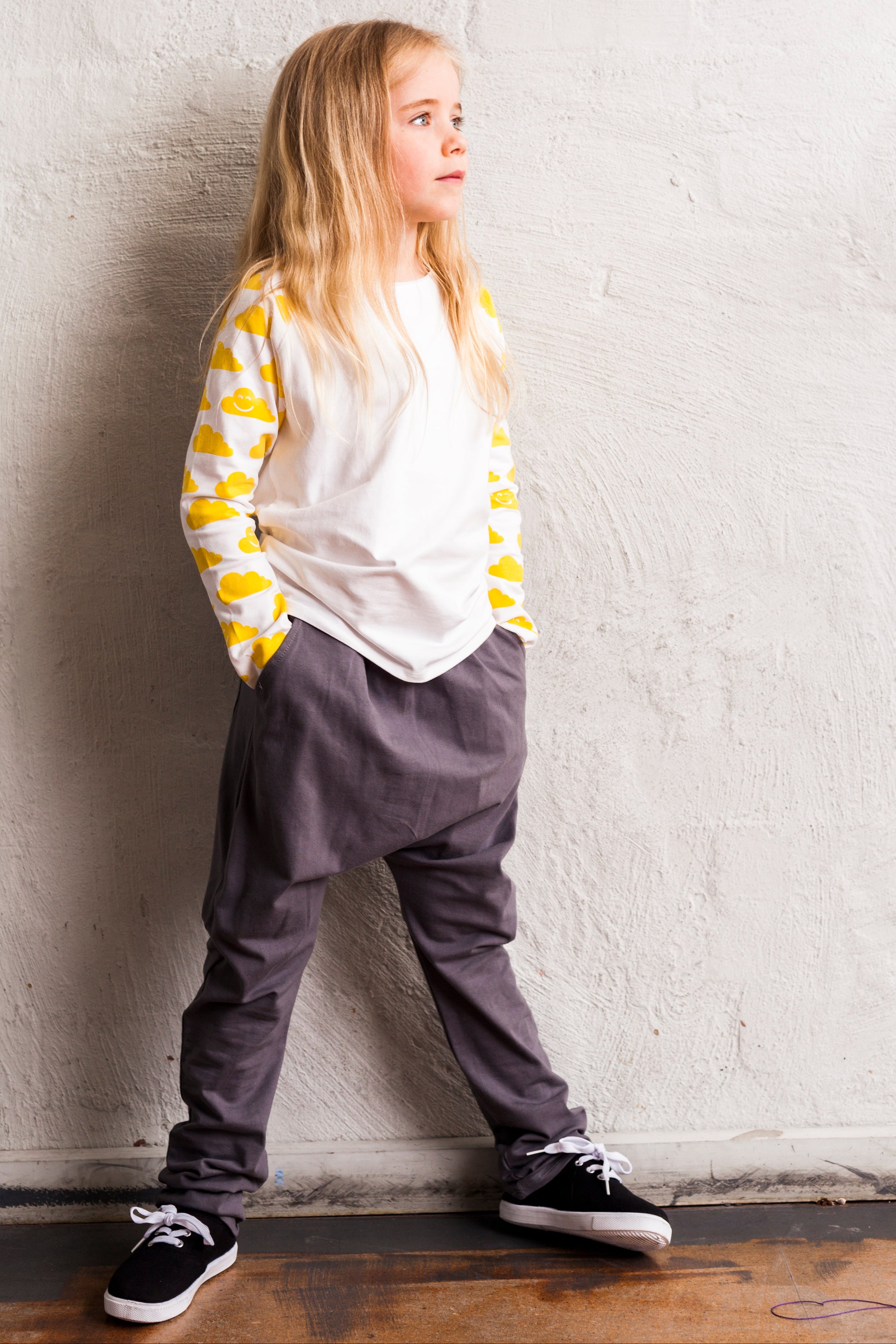 Child wearing a yellow and white striped shirt with gray pants against a white wall.