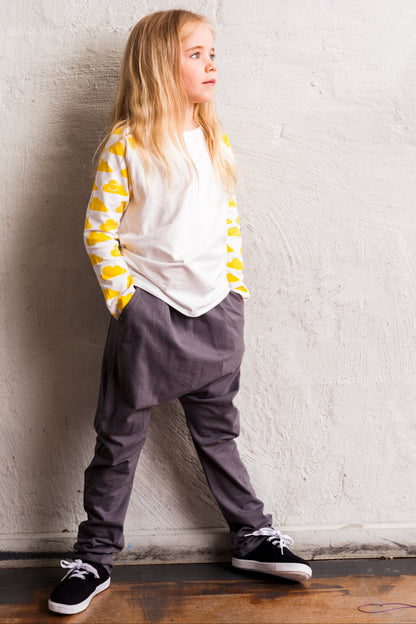 Child wearing a yellow and white striped shirt with gray pants against a white wall.