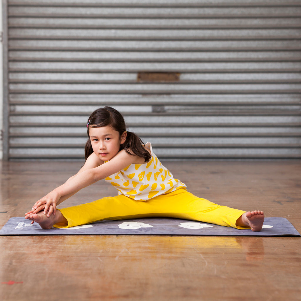 Young girl in a yellow outfit stretching on a mat in front of a metal shutter.