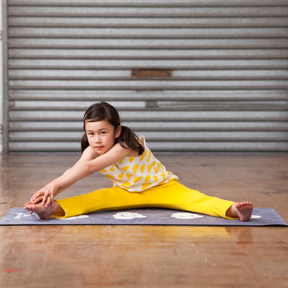 Young girl in a yellow outfit stretching on a mat in front of a metal shutter.