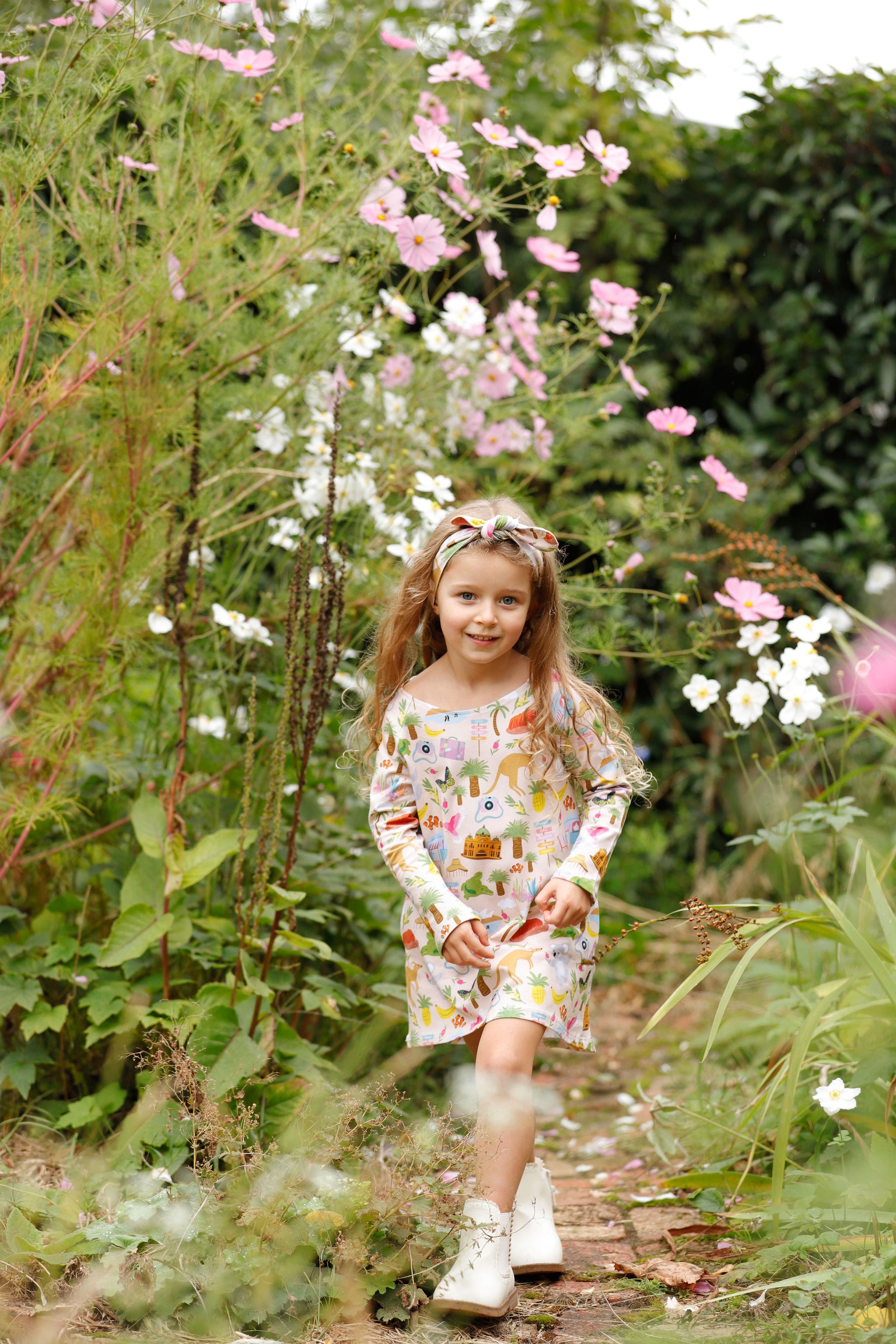 Little girl wearing Aussie Road Trip Australian print dress and matching headband walking through a flower garden.