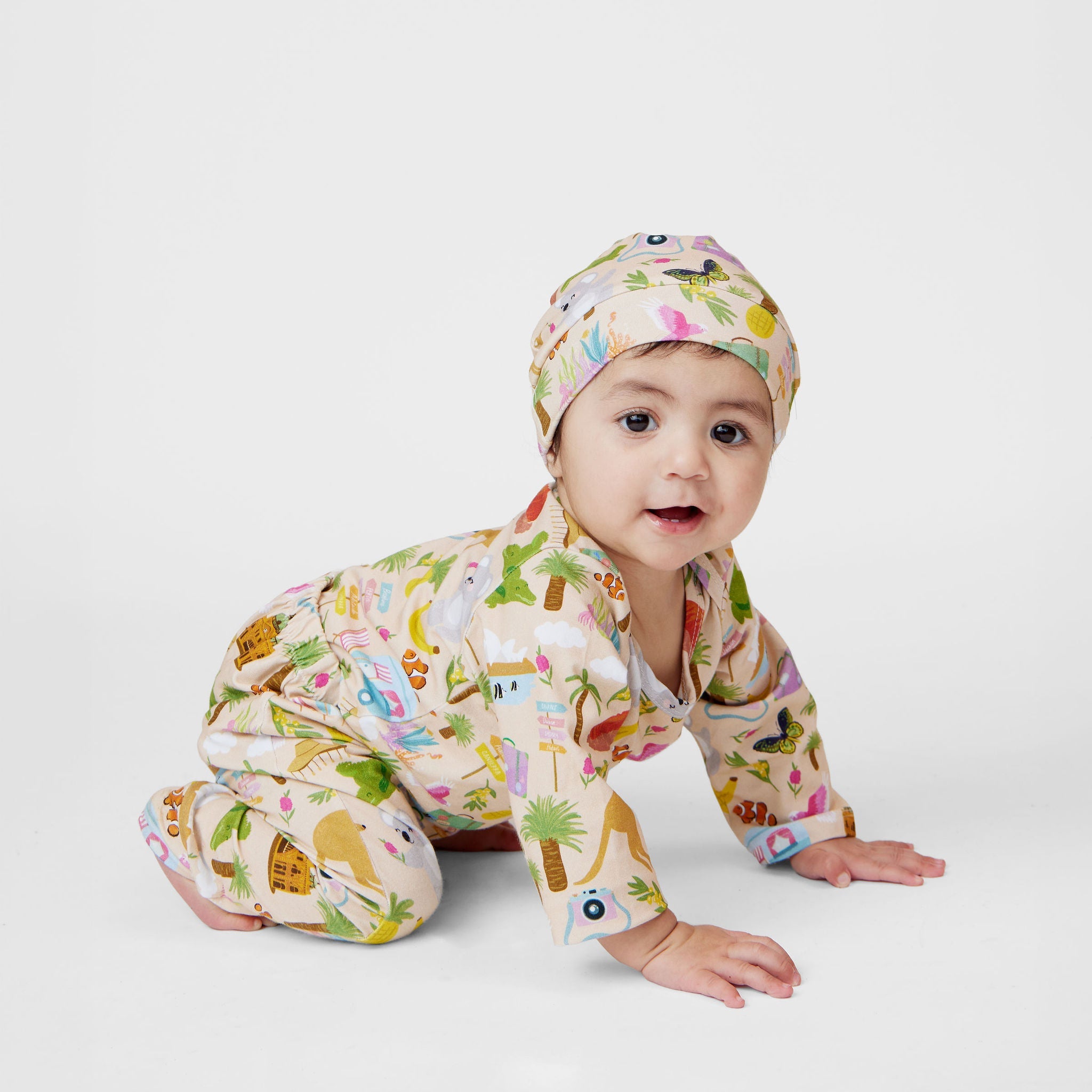 Baby wearing a Pebble and Poppet Aussie Road Trip organic cotton beanie and matching outfit while playing with a koala teething toy on a white background