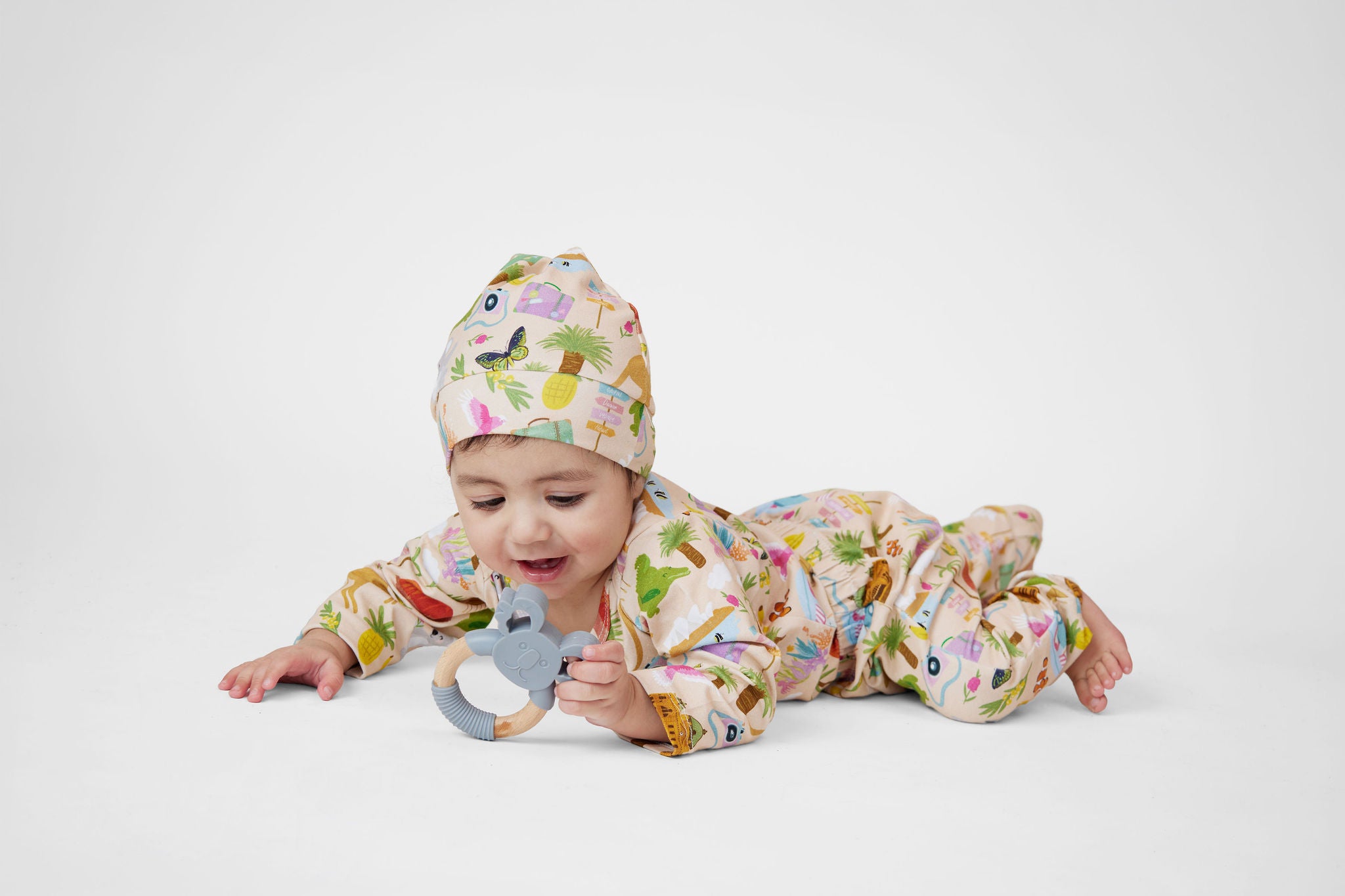 Baby wearing a Pebble and Poppet Aussie Road Trip organic cotton beanie and matching outfit while playing with a koala teething toy on a white background