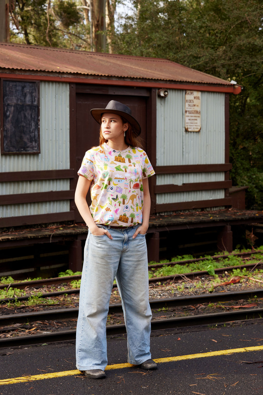 Model wearing Aussie Road Trip Australian print organic cotton t-shirt beside vintage railway building.