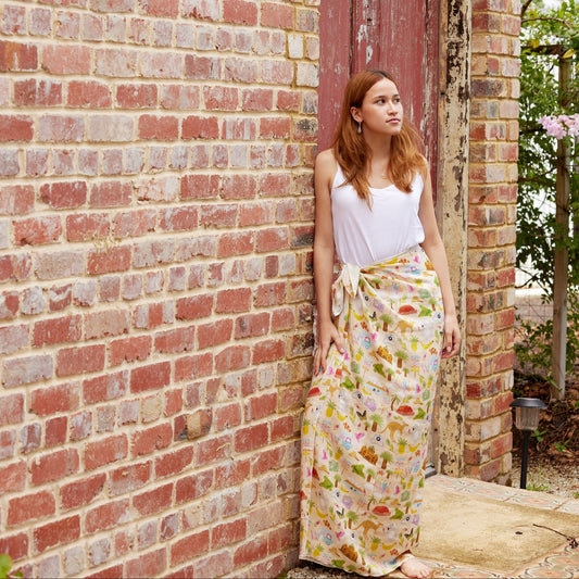 Young woman wearing the Aussie Road Trip print sarong by Christie Williams leaning against a rustic brick wall outdoors