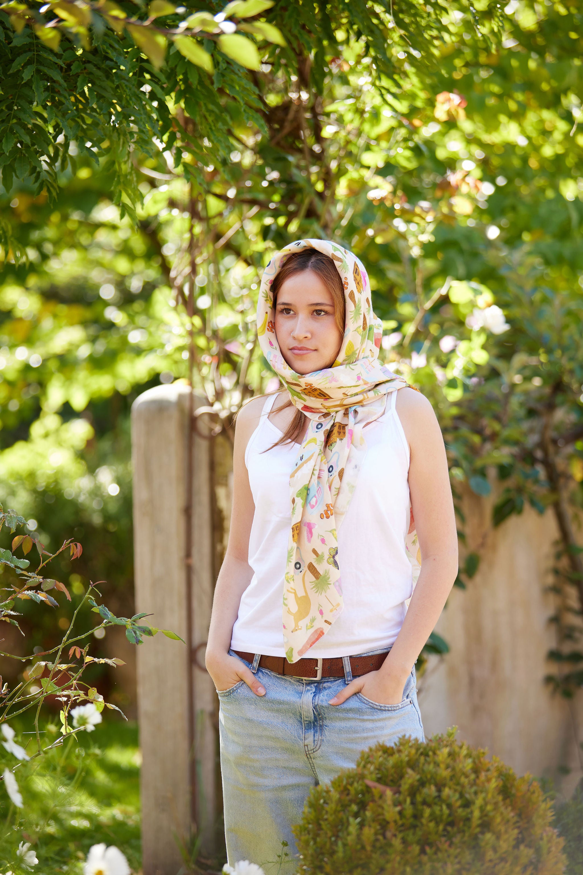 Young woman wearing the Christie Williams Aussie Road Trip scarf styled as a head wrap in a sunlit garden