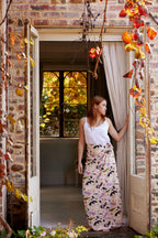 Young woman wearing an Australian bird print sarong styled with a white tank top standing in a rustic doorway with autumn vines