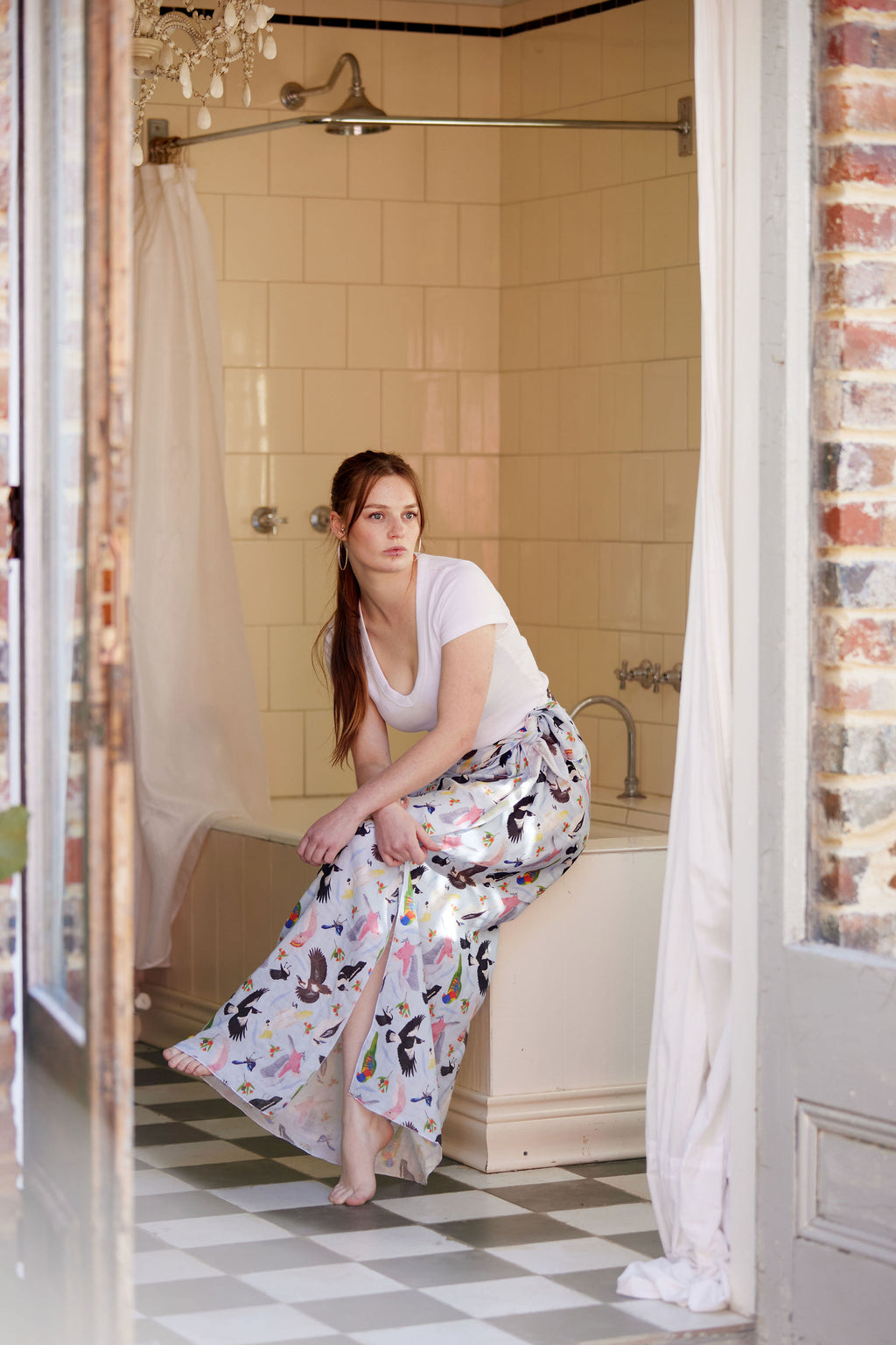 Woman wearing a flowing Australian bird print sarong in a vintage bathroom styled with a white fitted tee.