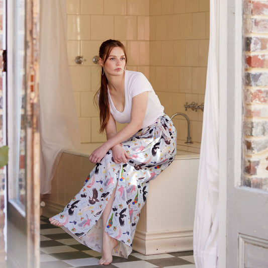 Woman wearing a flowing Australian bird print sarong in a vintage bathroom styled with a white fitted tee.