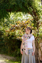 Young woman wearing a soft Australian bird print scarf standing beneath a leafy garden arch in warm sunlight