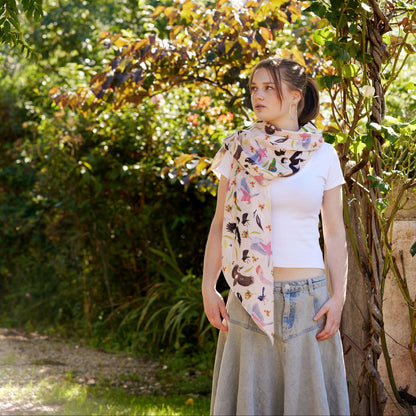 Young woman wearing a soft Australian bird print scarf standing beneath a leafy garden arch in warm sunlight