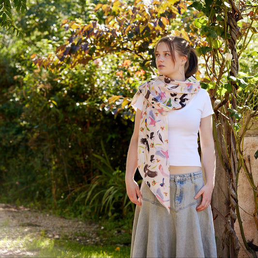 Young woman wearing a soft Australian bird print scarf standing beneath a leafy garden arch in warm sunlight