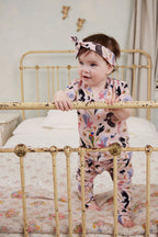 Baby standing in vintage iron bed wearing Backyard Birds baby pants and matching Australian bird print top with knotted headband