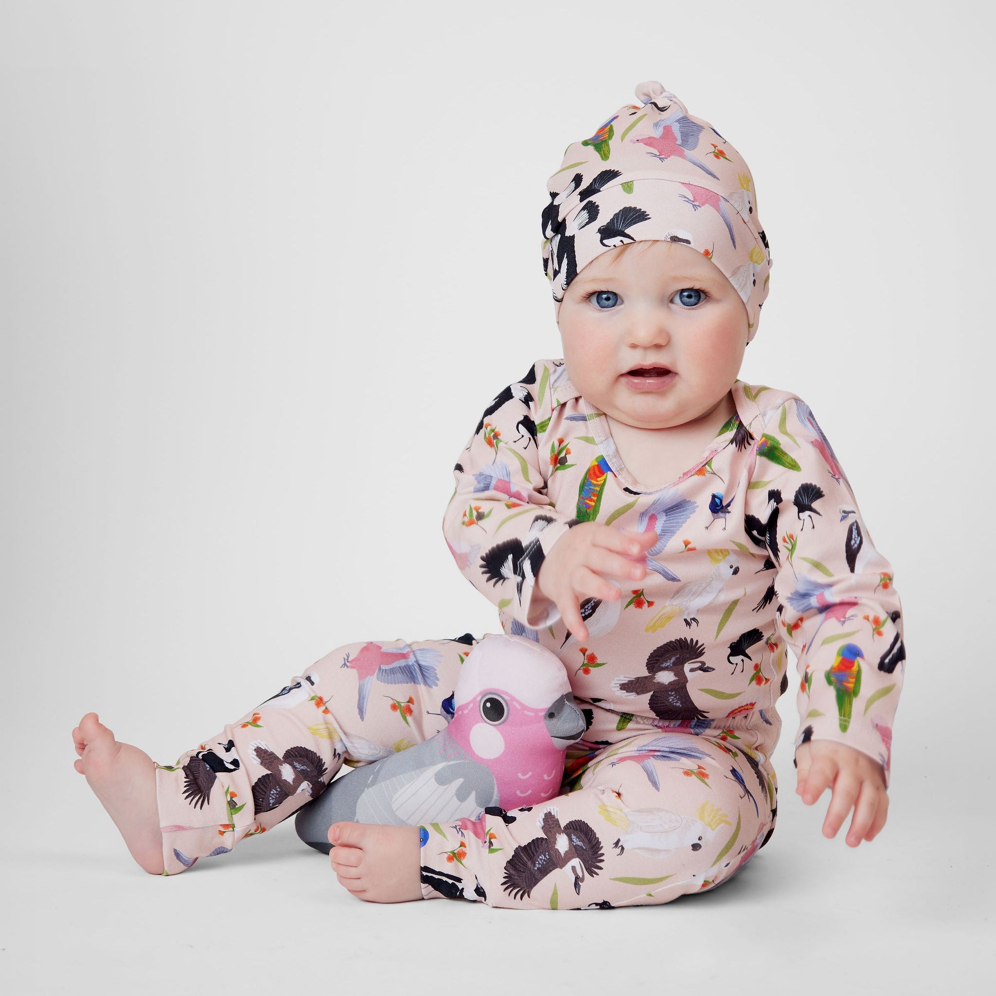 Baby wearing blush pink Backyard Birds romper and matching beanie with Australian bird illustrations