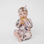Baby wearing blush pink Australian bird print romper with matching knotted headband holding teether toy