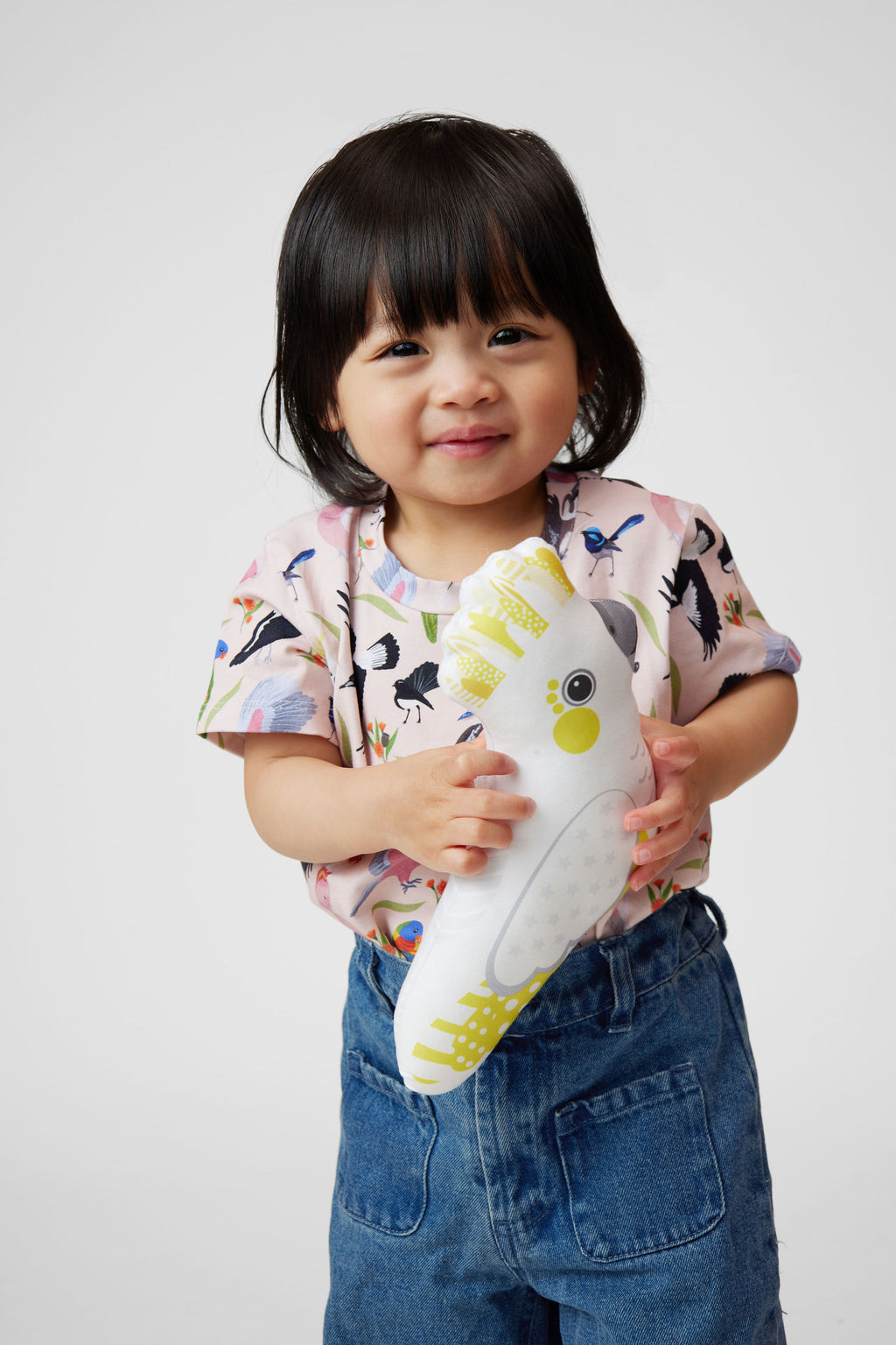 Toddler holding plush cockatoo toy while wearing Backyard Birds Australian bird print tee