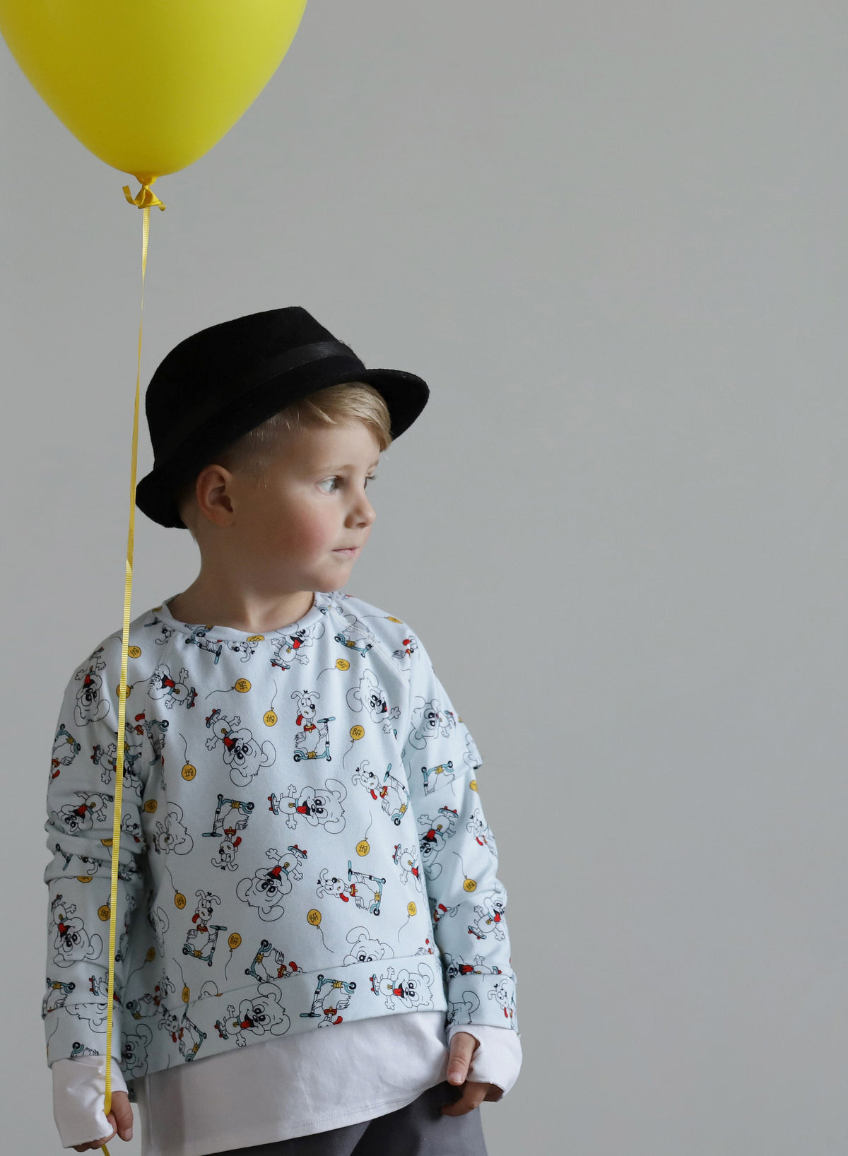 Young boy wearing a soft organic cotton puppy print sweater with grey shorts and black hat