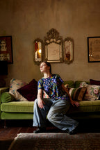 Model wearing Butterfly Flora organic cotton t-shirt sitting on green velvet couch in moody vintage interior.