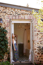 Woman wearing the Butterfly Flora bamboo scarf by Christie Williams styled as a flowing sarong in a rustic bathroom doorway