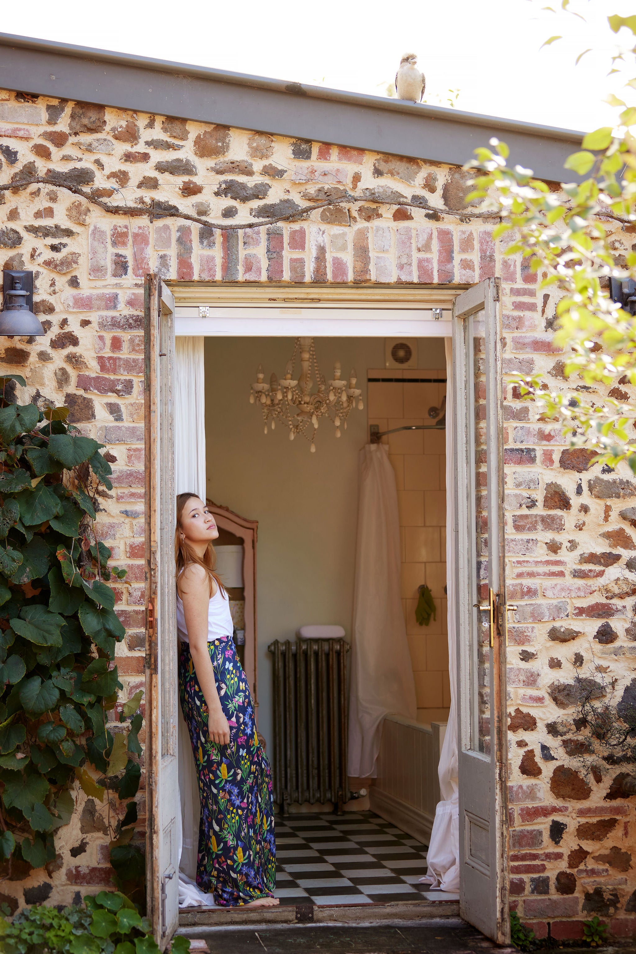 Woman wearing the Butterfly Flora bamboo scarf by Christie Williams styled as a flowing sarong in a rustic bathroom doorway