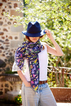 Woman styling the Butterfly Flora bamboo scarf with a navy felt hat in a sunlit garden setting