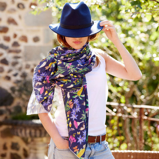Woman styling the Butterfly Flora bamboo scarf with a navy felt hat in a sunlit garden setting
