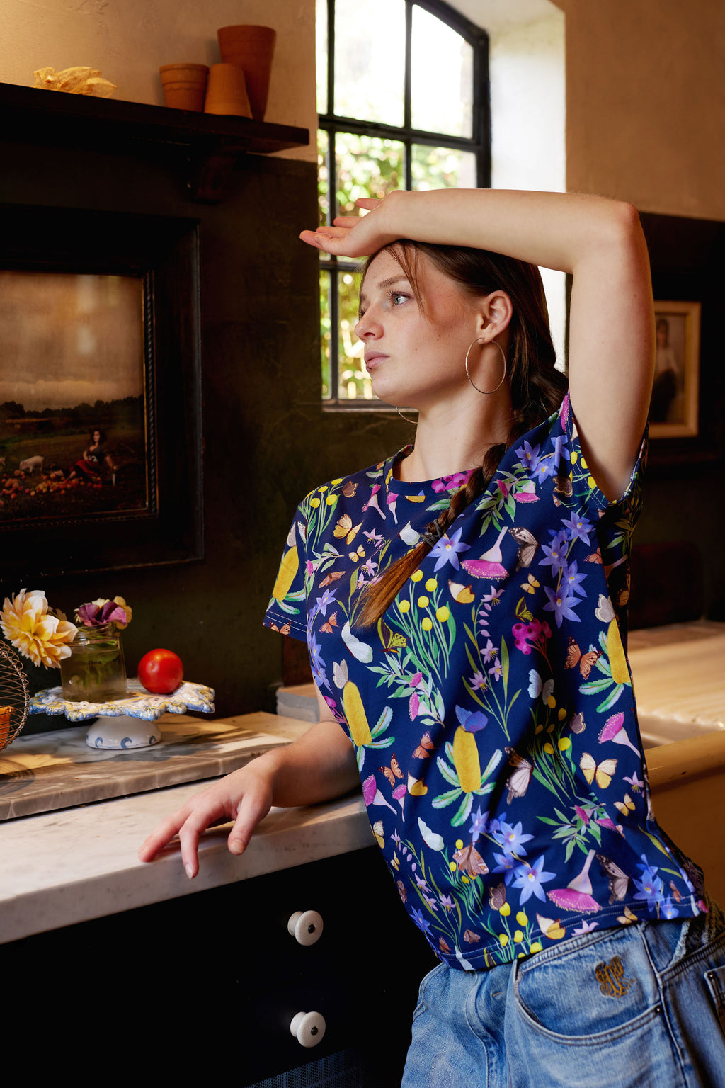 Close-up portrait of model wearing Butterfly Flora botanical print organic cotton t-shirt indoors beside window.