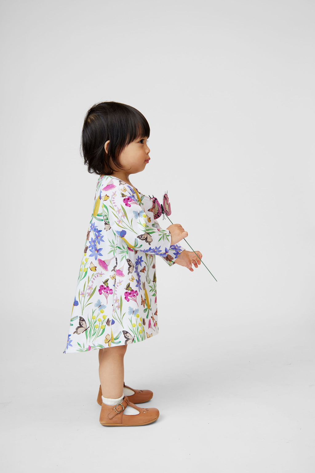 Little girl wearing Butterfly Flora long sleeve organic cotton dress holding butterfly flowers in a studio setting