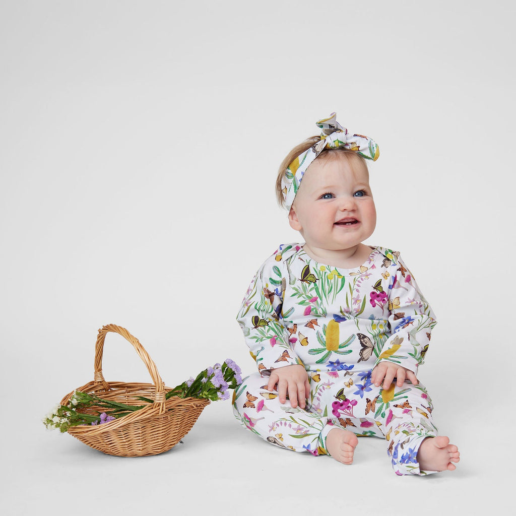 Baby wearing Butterfly Flora Australian made organic cotton leggings, long sleeve top and matching headband beside a wicker basket of flowers.