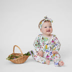 Baby wearing Butterfly Flora Australian made organic cotton leggings, long sleeve top and matching headband beside a wicker basket of flowers.