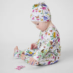 Baby wearing Butterfly Flora Australian made organic cotton romper and matching knot beanie sitting beside a butterfly toy.
