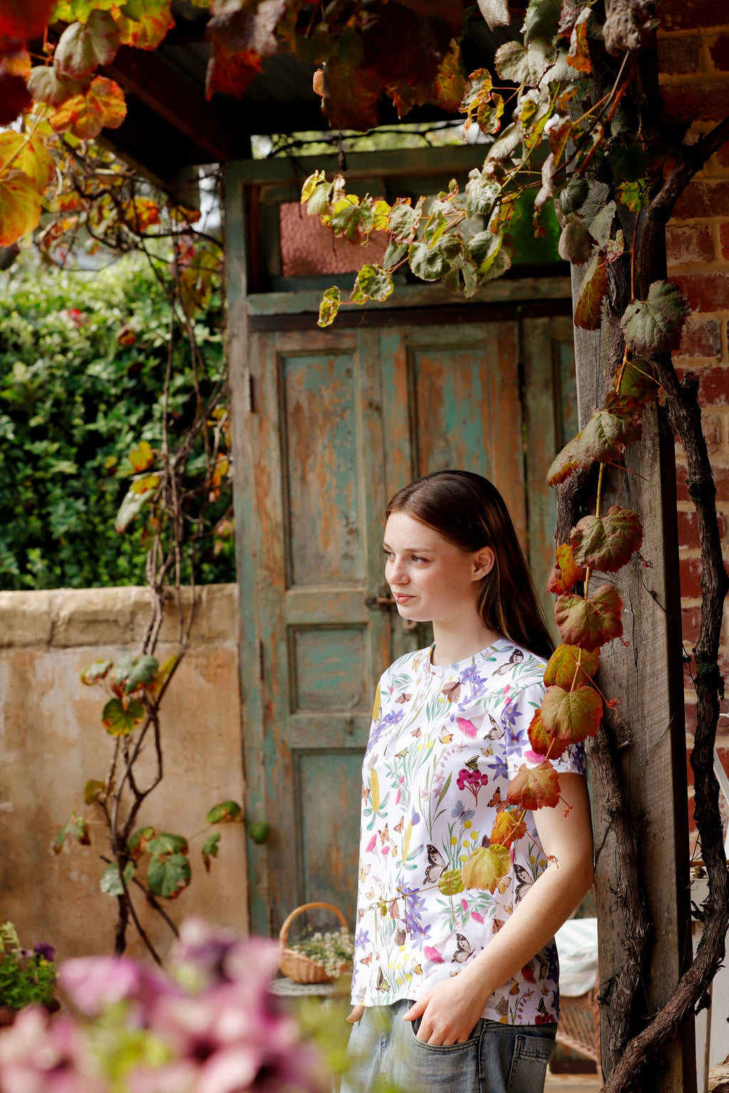 Portrait of model wearing Butterfly Flora White floral butterfly print t-shirt in vintage doorway.