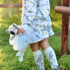 Girl wearing puppy print wrap skirt and matching organic cotton outfit outdoors holding a soft toy koala
