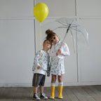 Boy and girl wearing puppy print organic cotton outfits with yellow balloon and clear umbrella