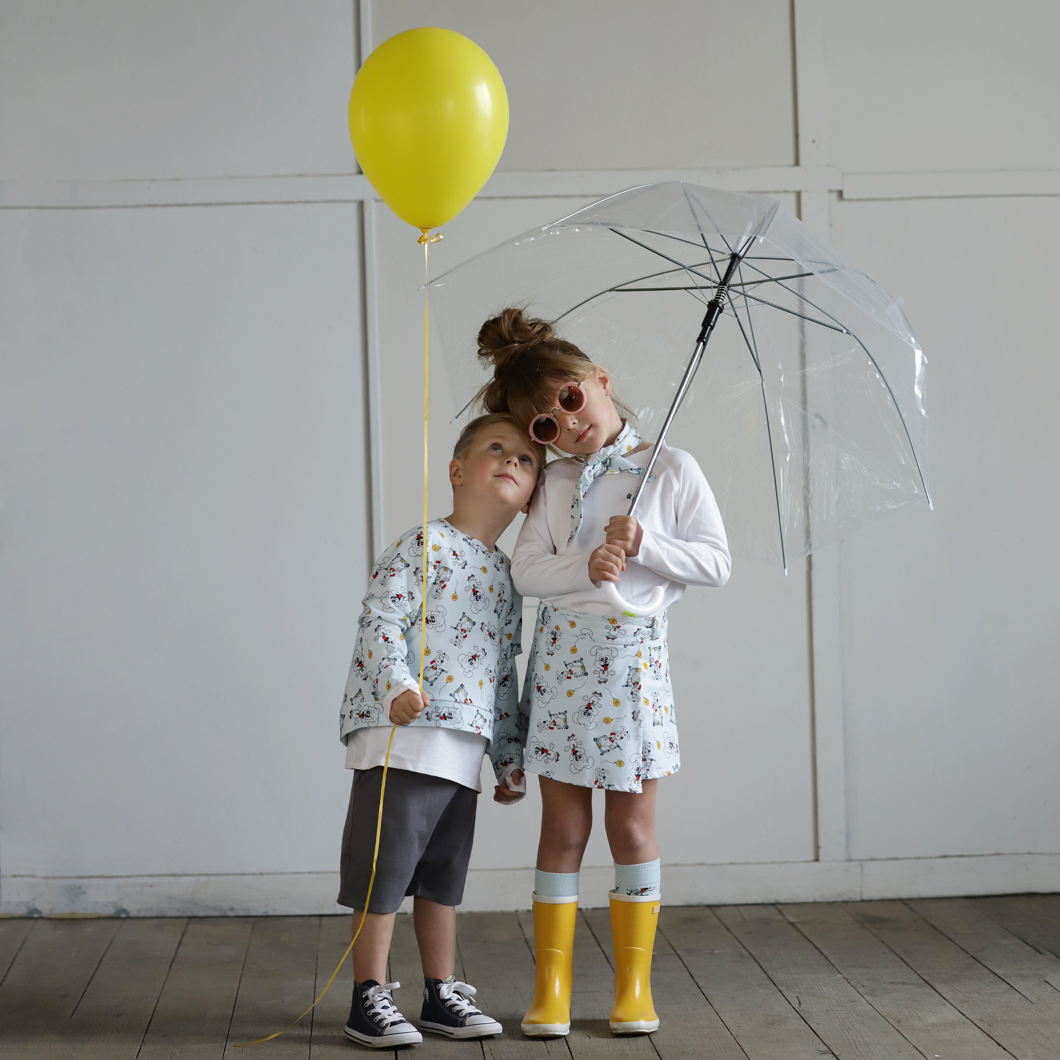 Boy and girl wearing puppy print organic cotton outfits with yellow balloon and clear umbrella