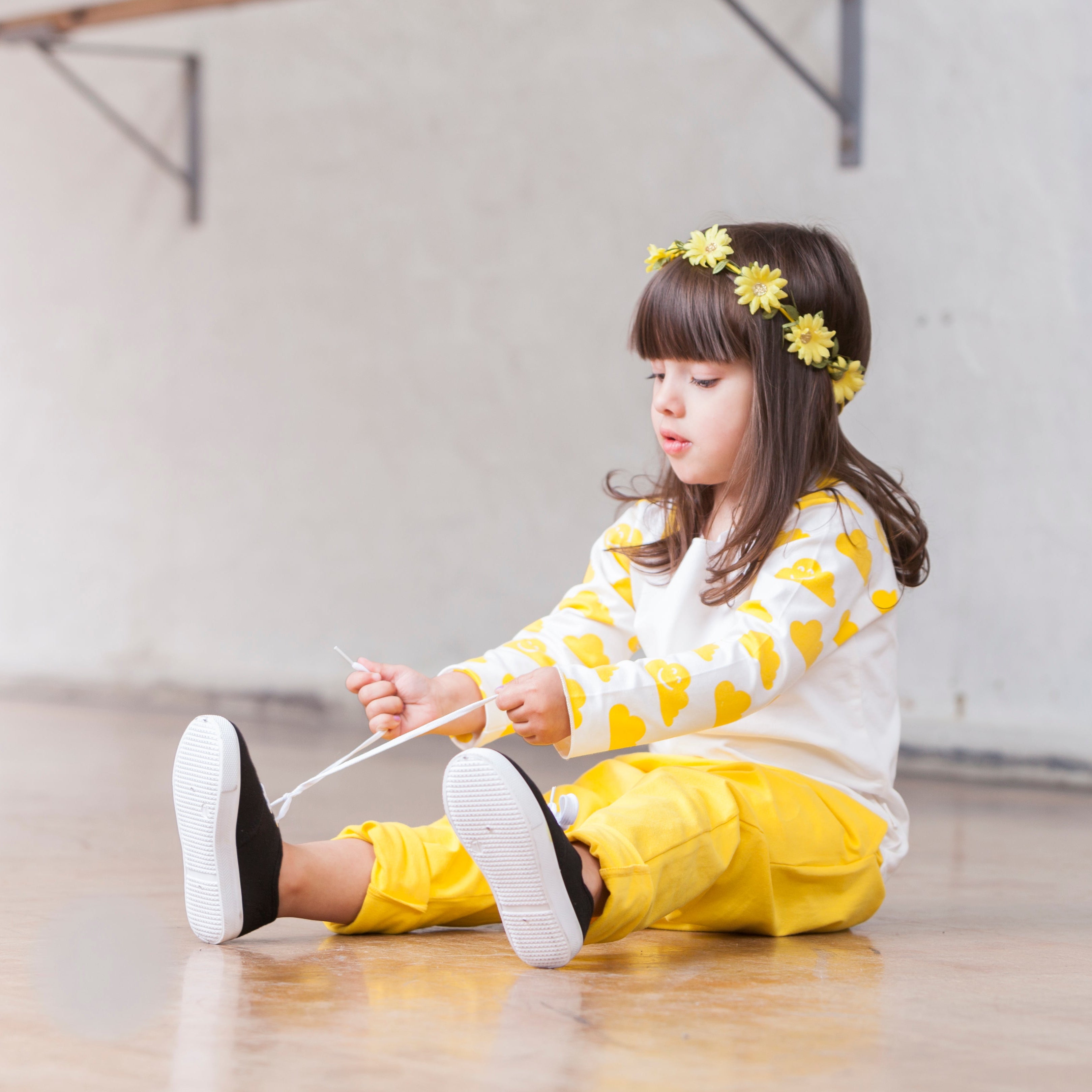Child sitting on the floor wearing a yellow and white outfit with flower headband.
