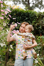 Mother and baby wearing matching Aussie Road Trip organic cotton outfits surrounded by flowers in garden.