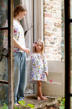 Mother and child wearing matching Butterfly Flora floral butterfly outfits beside rustic cottage doorway.