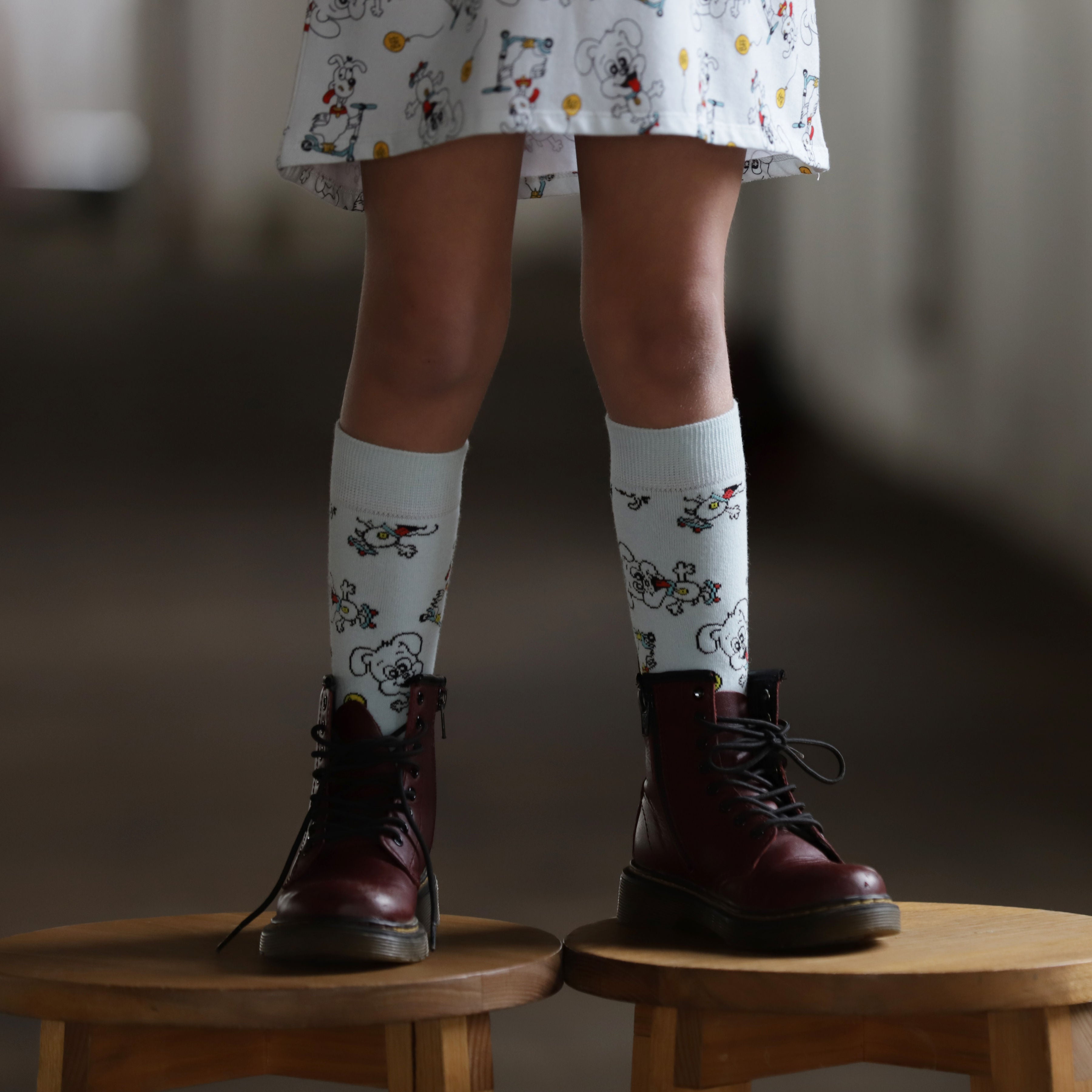 Young girl wearing patterned socks and dark boots on a wooden stool with a blurred background