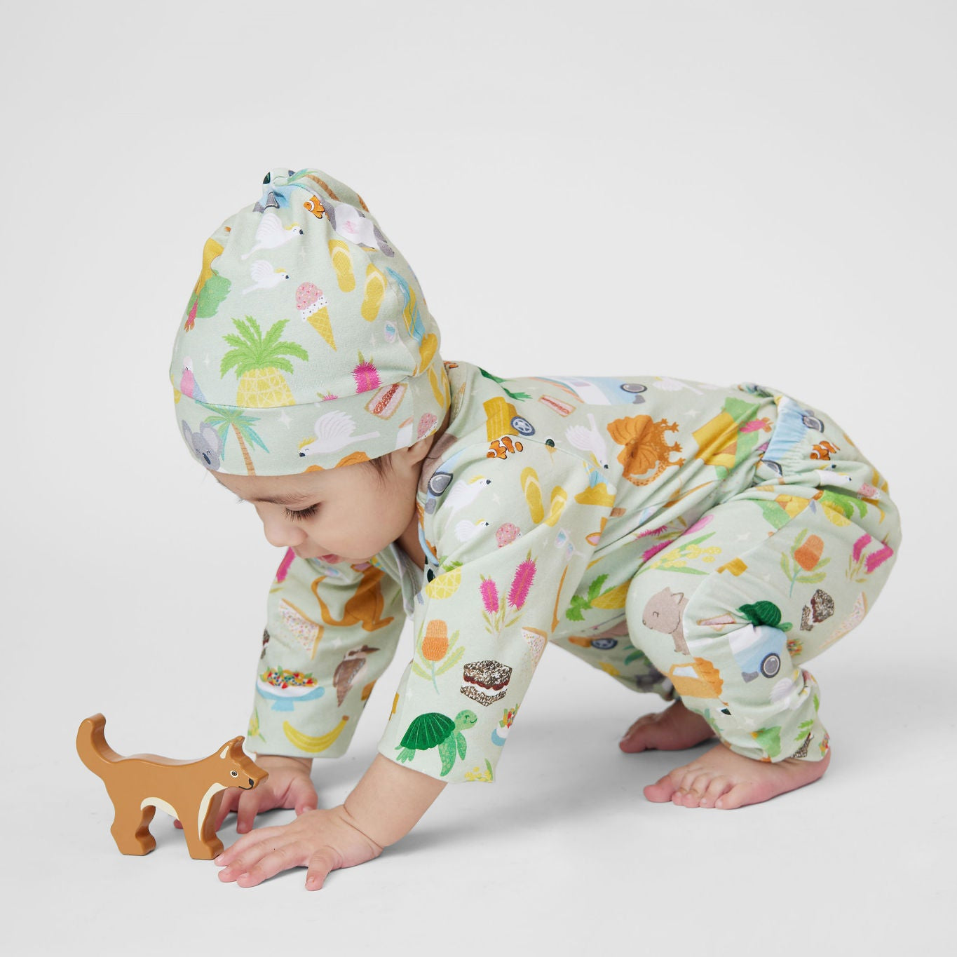 Baby wearing Summer Down Under organic cotton romper and matching beanie featuring nostalgic Australian summer illustrations including caravans, kangaroos, palm trees and beach adventures