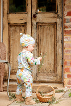 Baby wearing Pebble and Poppet Summer Down Under organic cotton beanie and matching outfit holding wildflowers outside rustic cottage doors. Designed and made in Australia.