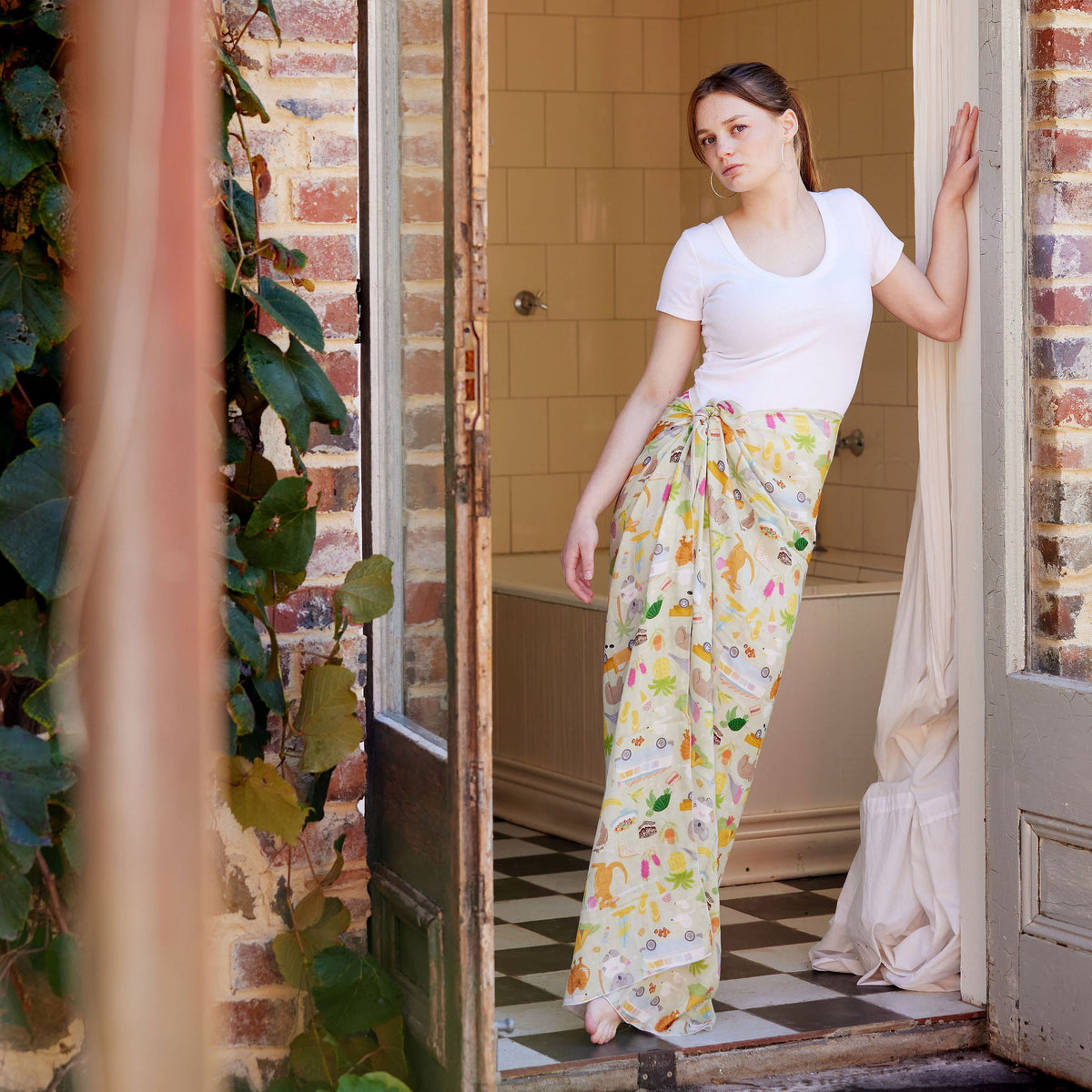 Young woman wearing the Summer Down Under bamboo scarf by Christie Williams styled as a sarong in a rustic Australian bathroom doorway