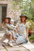 Mother and children wearing matching Pebble and Poppet Summer Down Under organic cotton outfits featuring whimsical Australian print with kangaroos, kombis and camping icons in cottage garden setting. Designed and made in Australia.